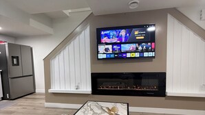 Ett vardagsrum med en platt-TV som är monterad på väggen, en öppen spis nedanför och ett soffbord i marmor i mitten av rummet.