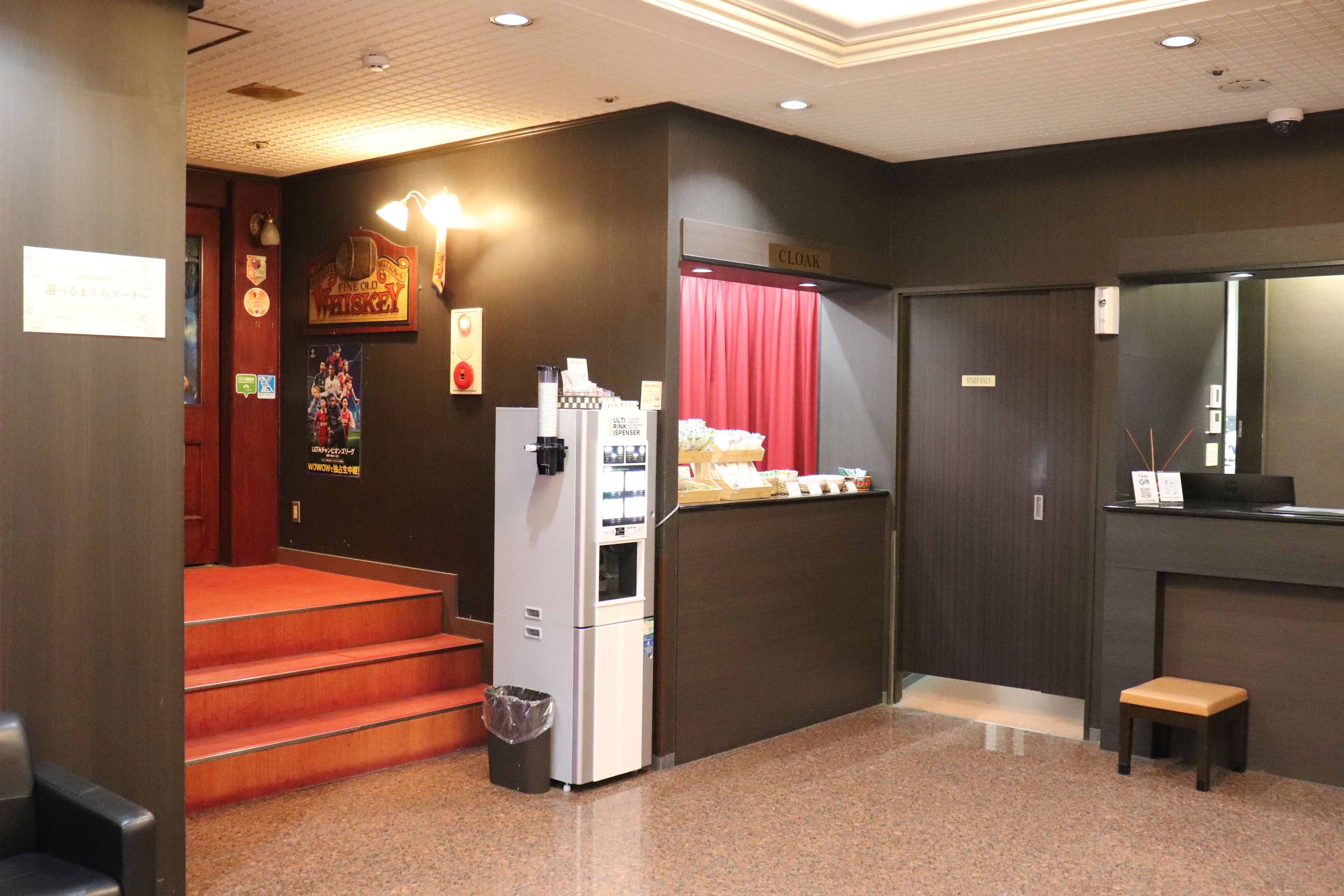 A hotel lobby with a reception desk, a vending machine, a trash can, and a small seating area.