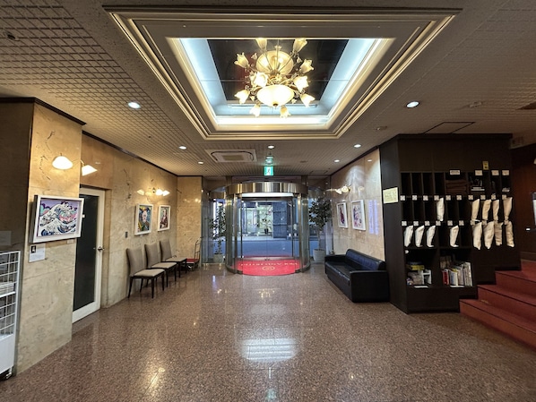 A hotel lobby with a central elevator, seating area, and a clothing rack.
