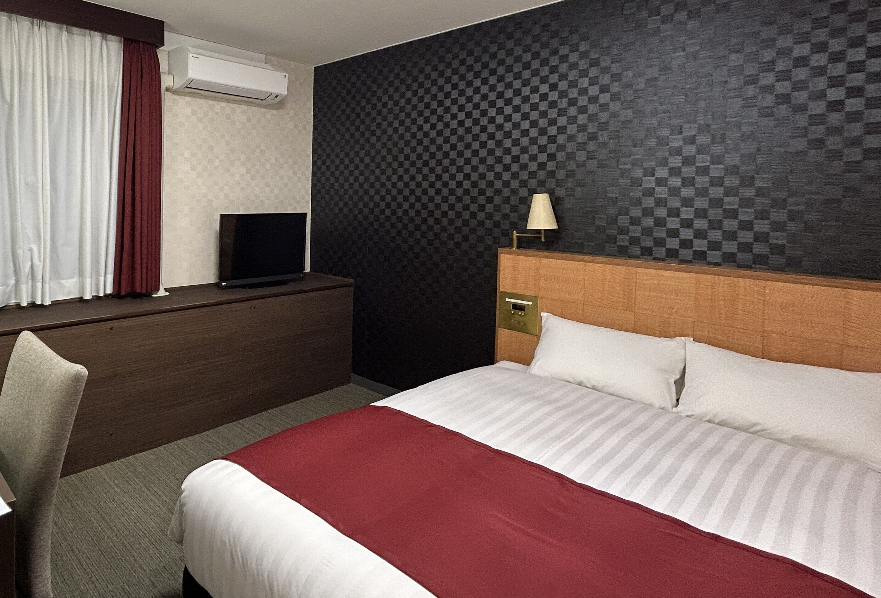 A hotel room with a bed, a desk with a TV, a lamp, and a checkered wall.