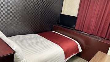 Ein Hotelzimmer mit kariertem Kopfteil, einem Bett mit rot-weißer Bettdecke, einem Fernseher auf einem Holztisch und einem roten Vorhang.