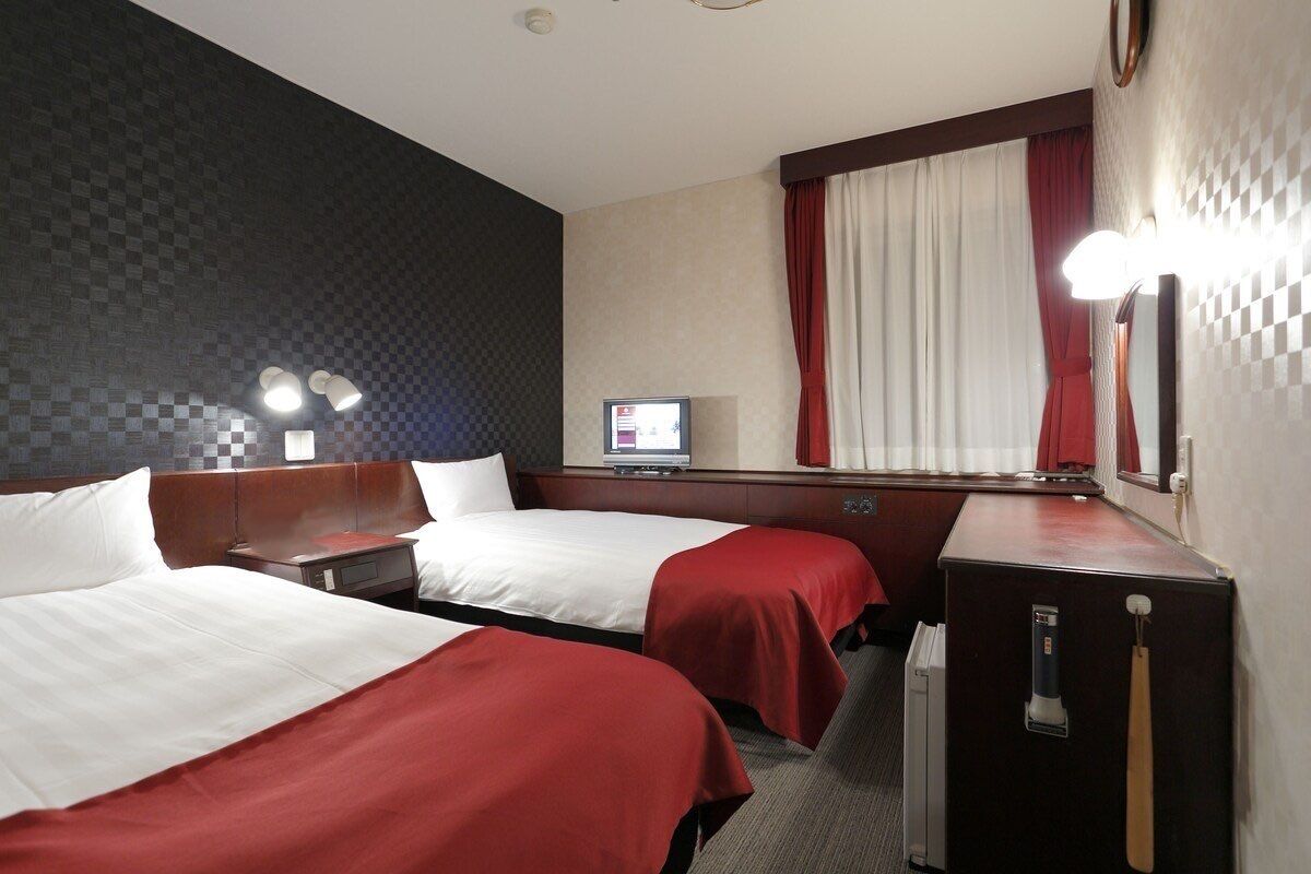 Hotelkamer met twee bedden, een bureau, een spiegel, een televisie en een raam met gordijnen.