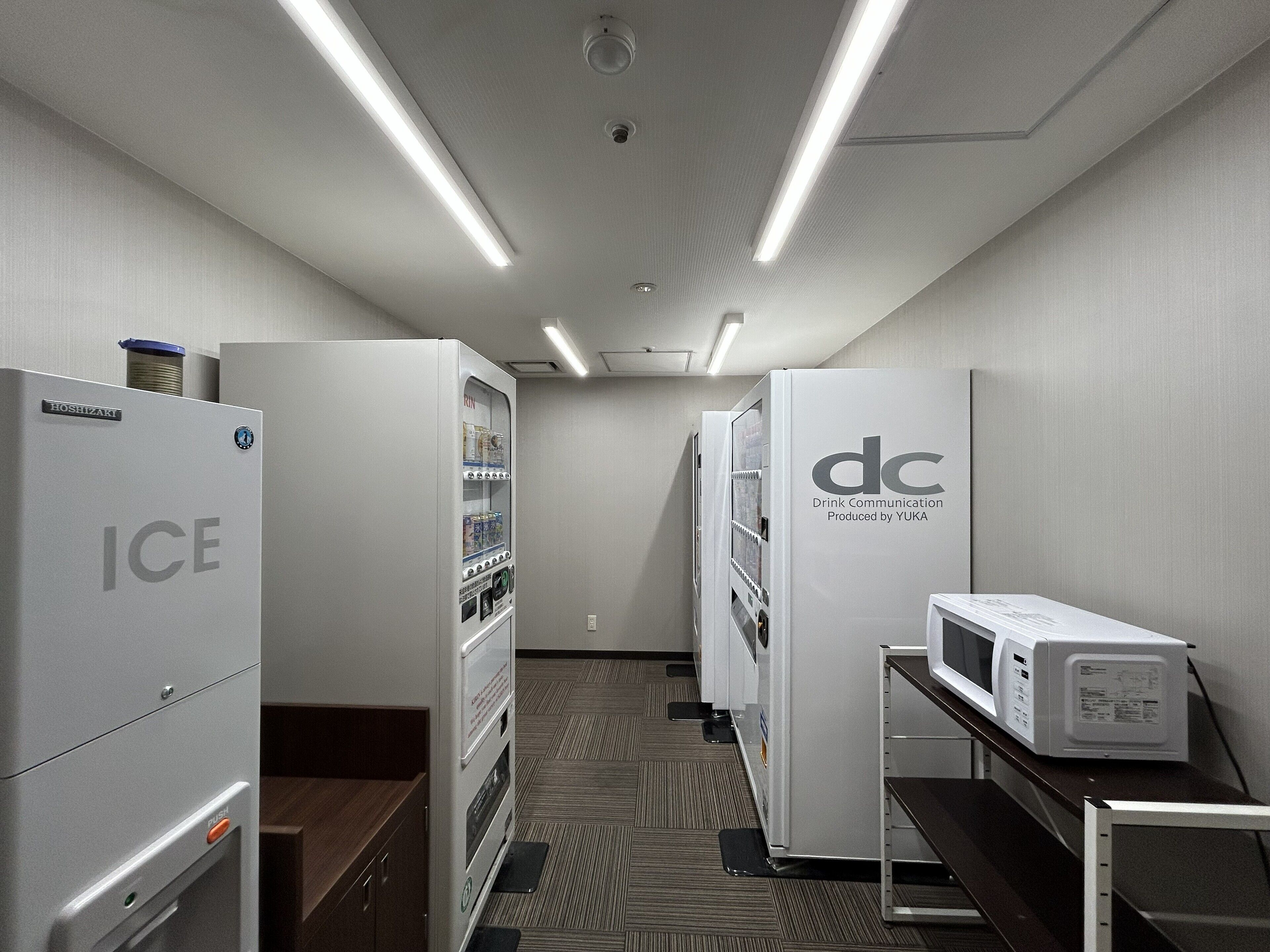 A corridor with vending machines labeled "ICE" and "dc" for drink communication, and a microwave on a counter.