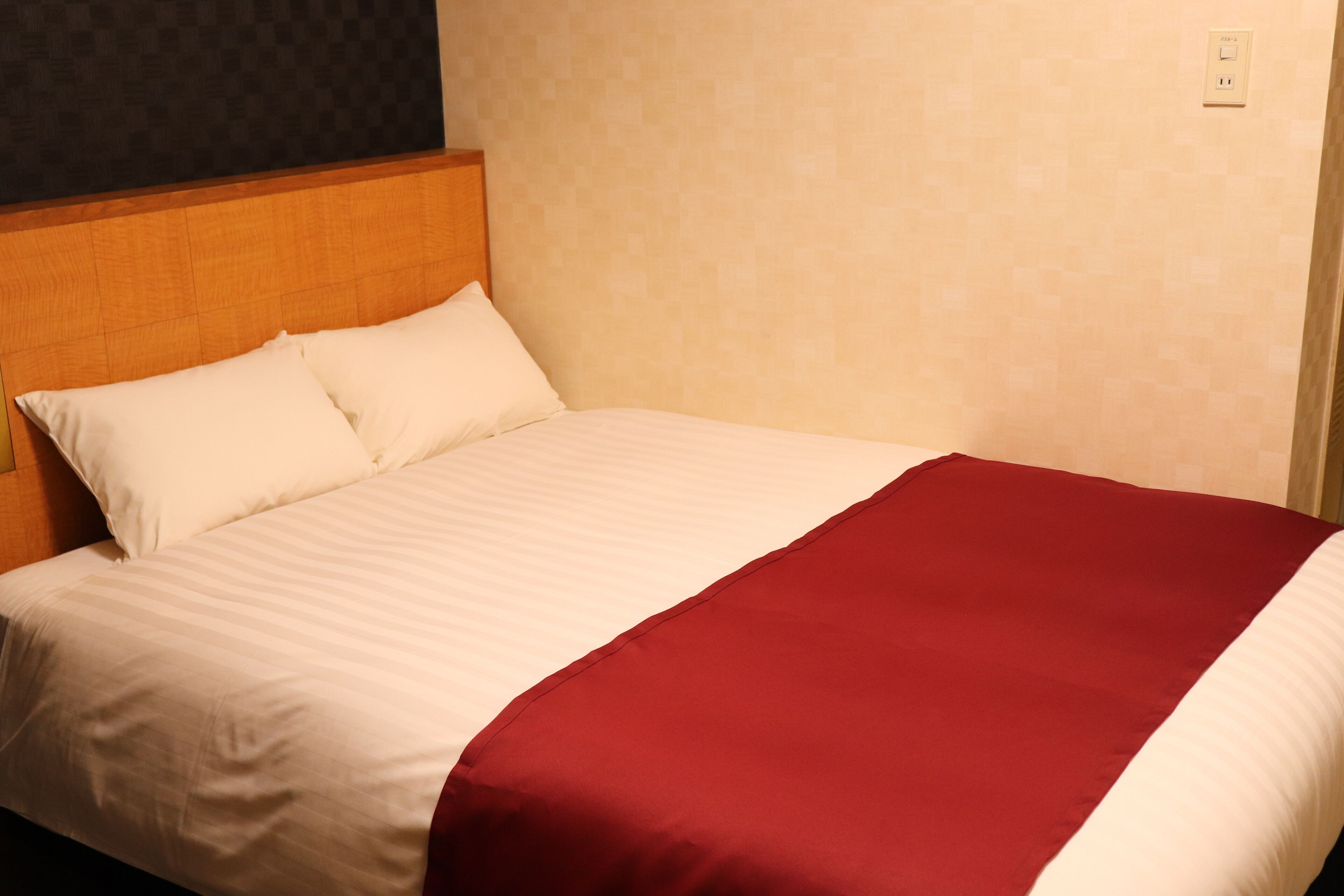 A neatly made bed with white and red bedding, a wooden headboard, and a patterned wall.