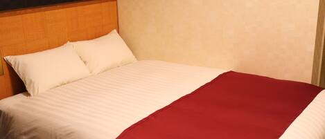 A neatly made bed with white and red bedding, a wooden headboard, and a patterned wall.