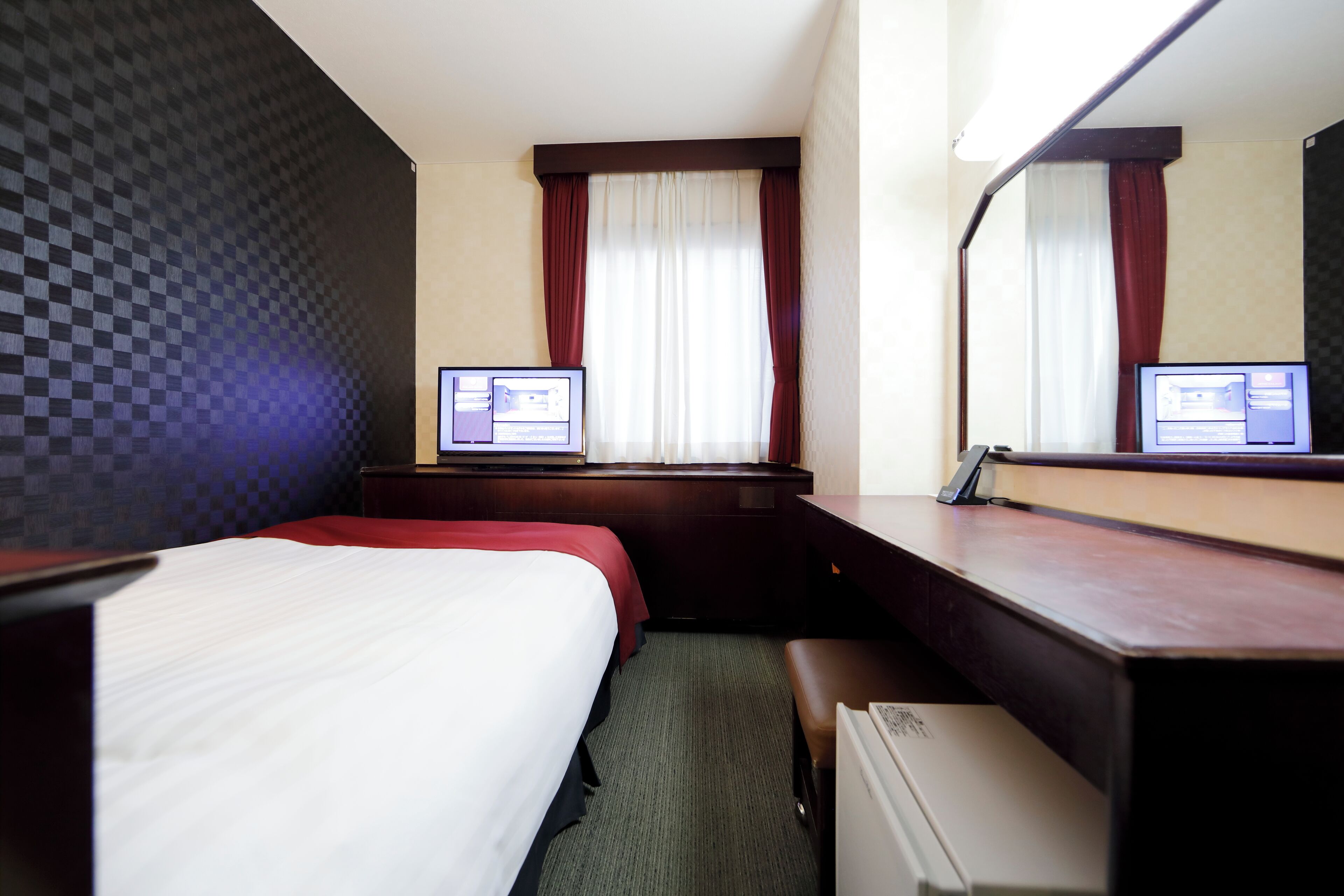 A hotel room with a bed, a desk, a computer, and a window with curtains.