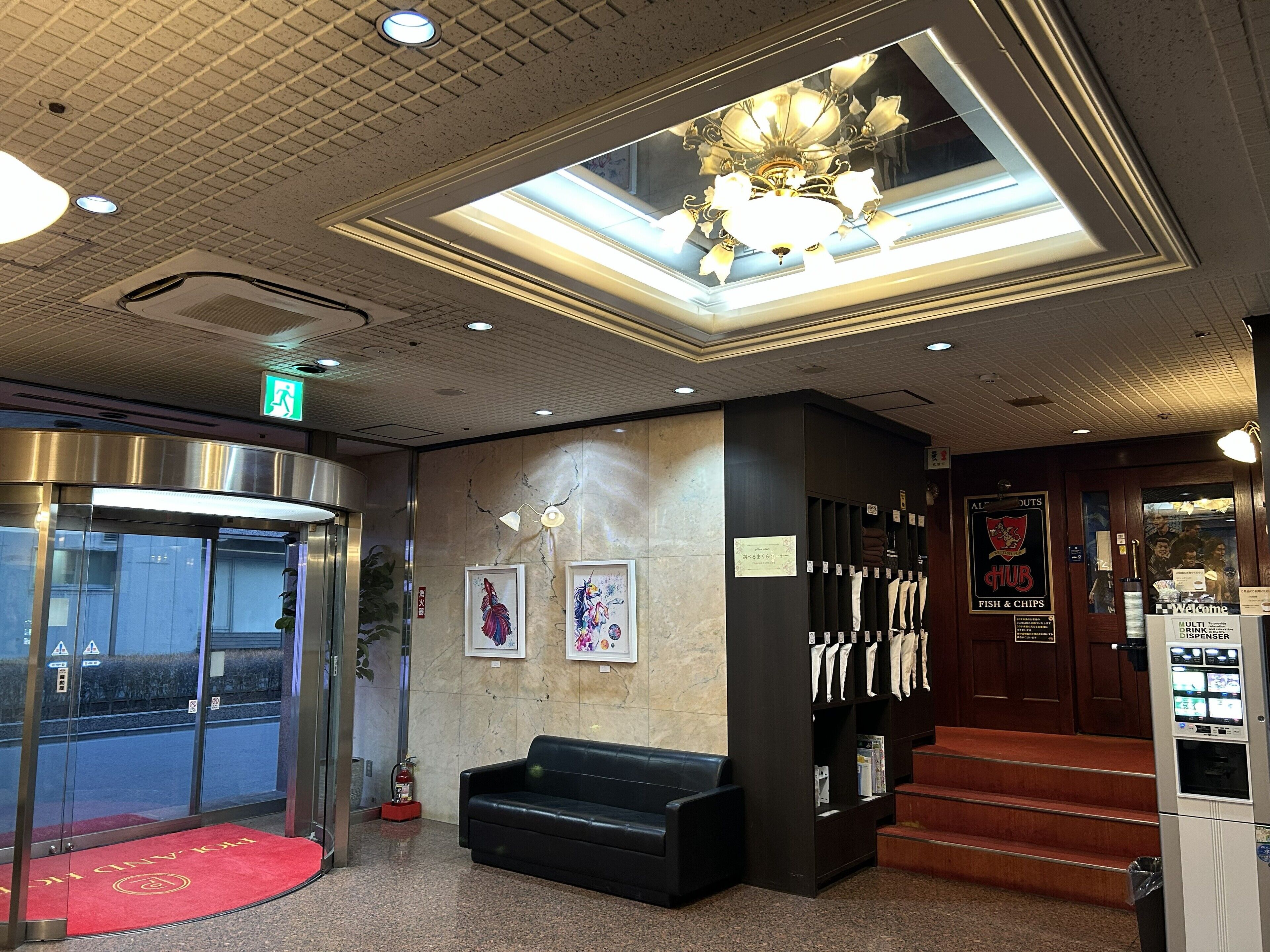 A lobby with a reception desk, a staircase, a fire extinguisher, and a wall with framed artwork.