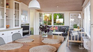 Una cocina moderna con armarios de madera, una mesa de comedor con individuales y vistas a un jardín a través de amplios ventanales.