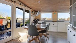 Una cocina moderna con techo de madera, ventanas amplias y un comedor con mesa y sillas.