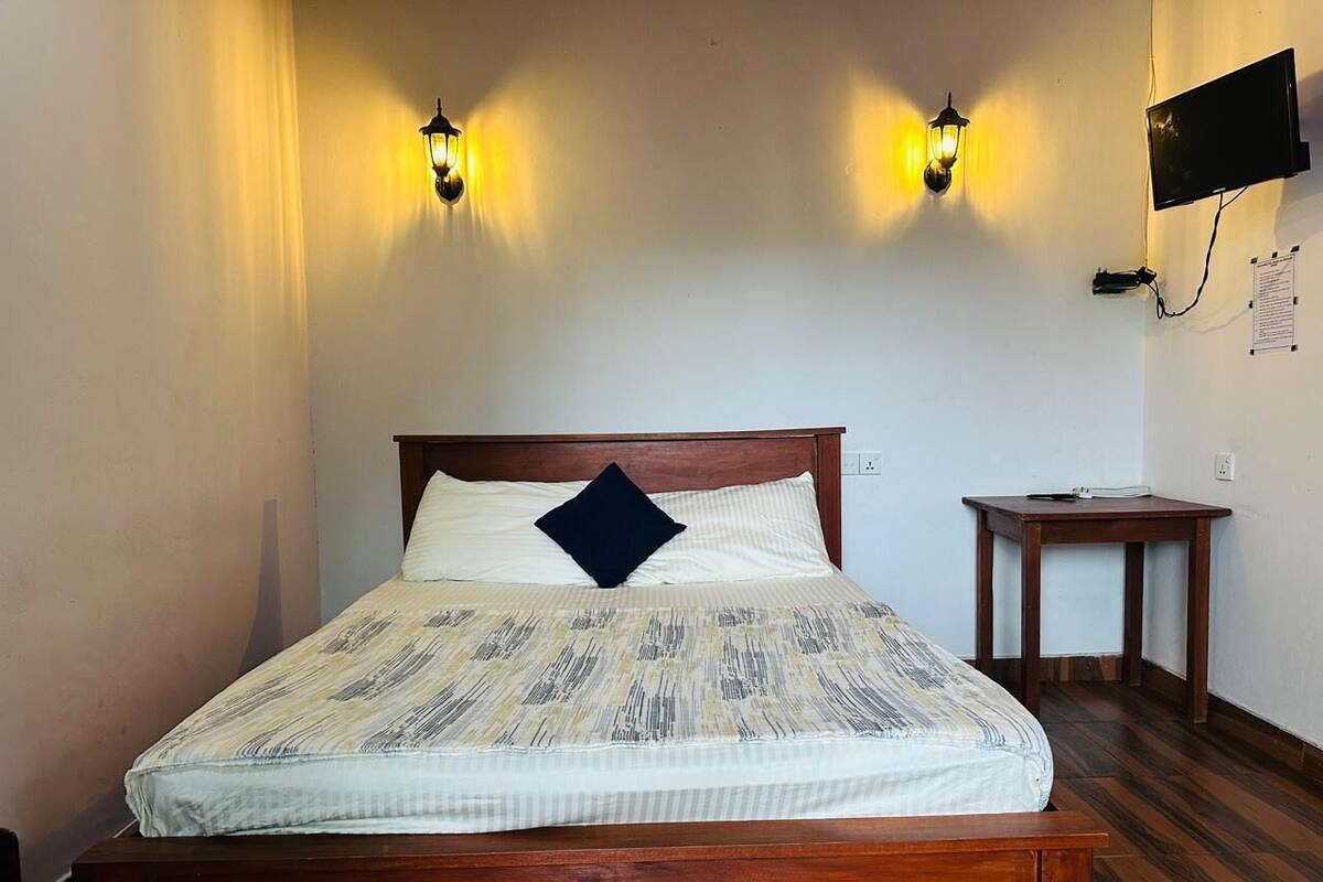 A neatly made bed with a patterned bedspread and a single pillow, flanked by two wall-mounted lamps.