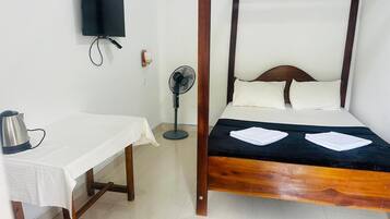 A room with a bed, a table, a kettle, a TV, and a fan.