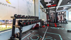 Een sportschool met een wandgemonteerde dumbbellhouder, gewichthefapparatuur en een vloer met geometrische patronen.
