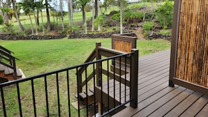 A wooden deck with a bamboo screen, a staircase leading to a deck, and a grassy area with trees.