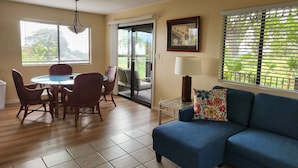 A living room with a blue sofa, a dining table with chairs, a lamp, and a picture on the wall.