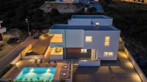 Ein modernes, zweistöckiges Gebäude mit Swimmingpool, Liegestühlen und gut beleuchteter Fassade.