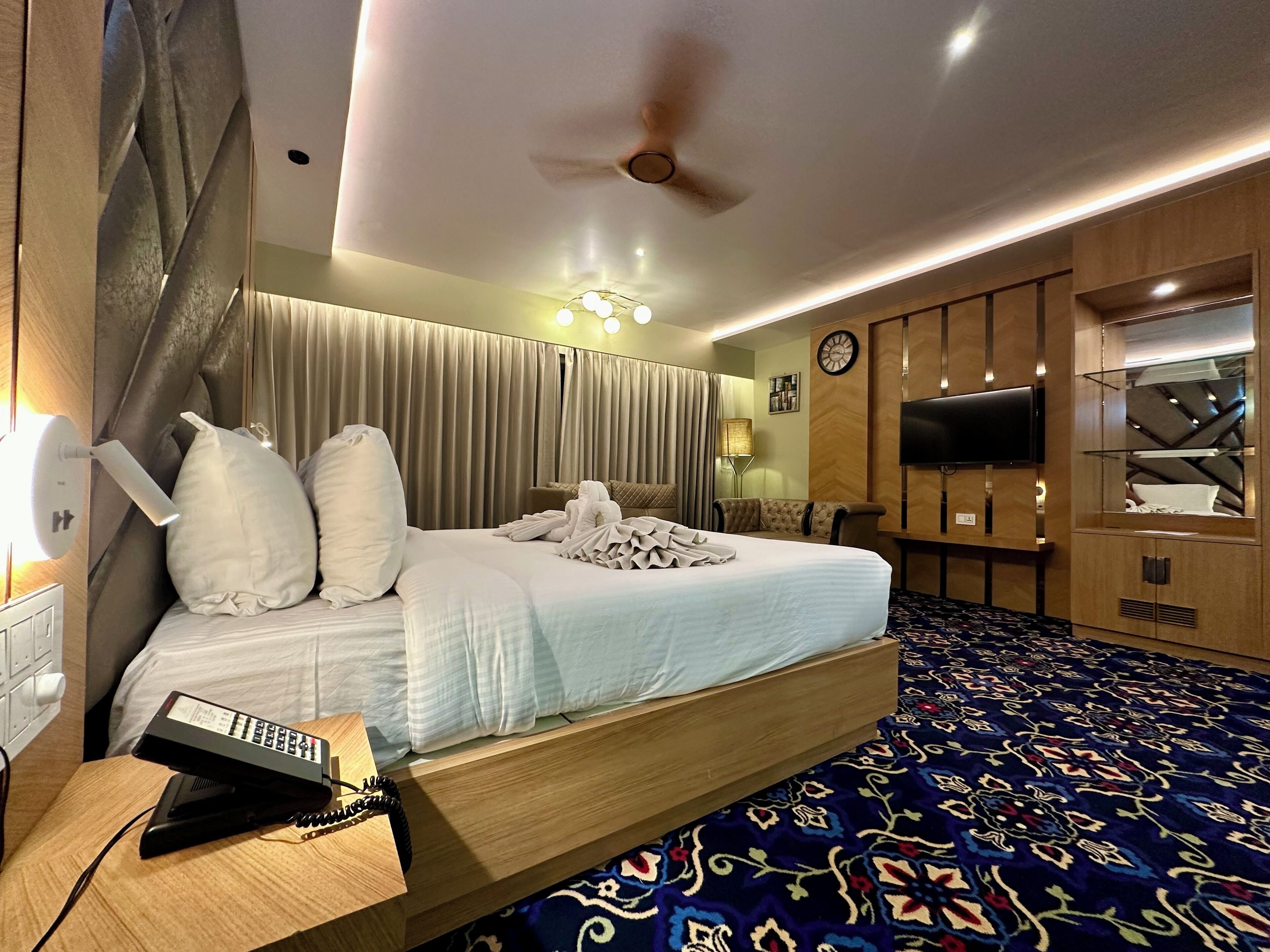 A hotel room with a large bed, a desk with a telephone, a television, and a clock on the wall.