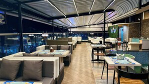 Un restaurante interior con mesas altas, asientos acolchados, una zona de piscina y vistas a la ciudad.
