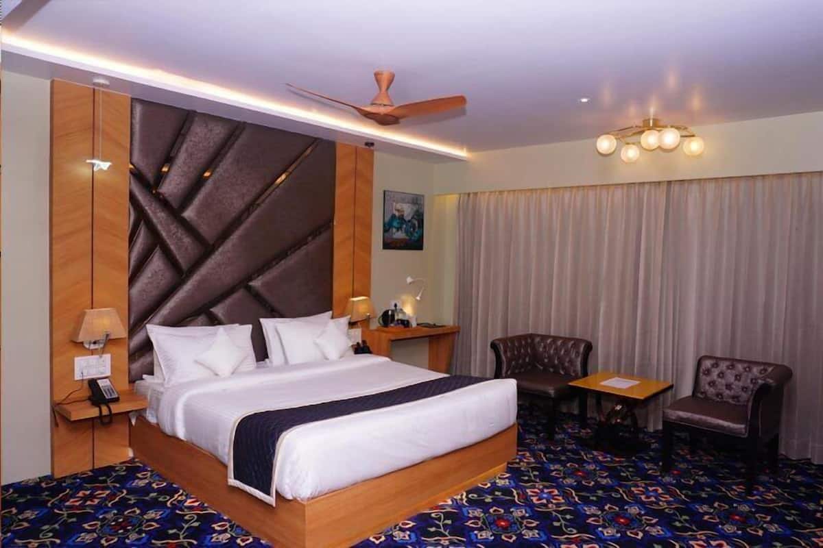 A hotel room with a large bed, a desk, two chairs, a ceiling fan, and a patterned carpet.
