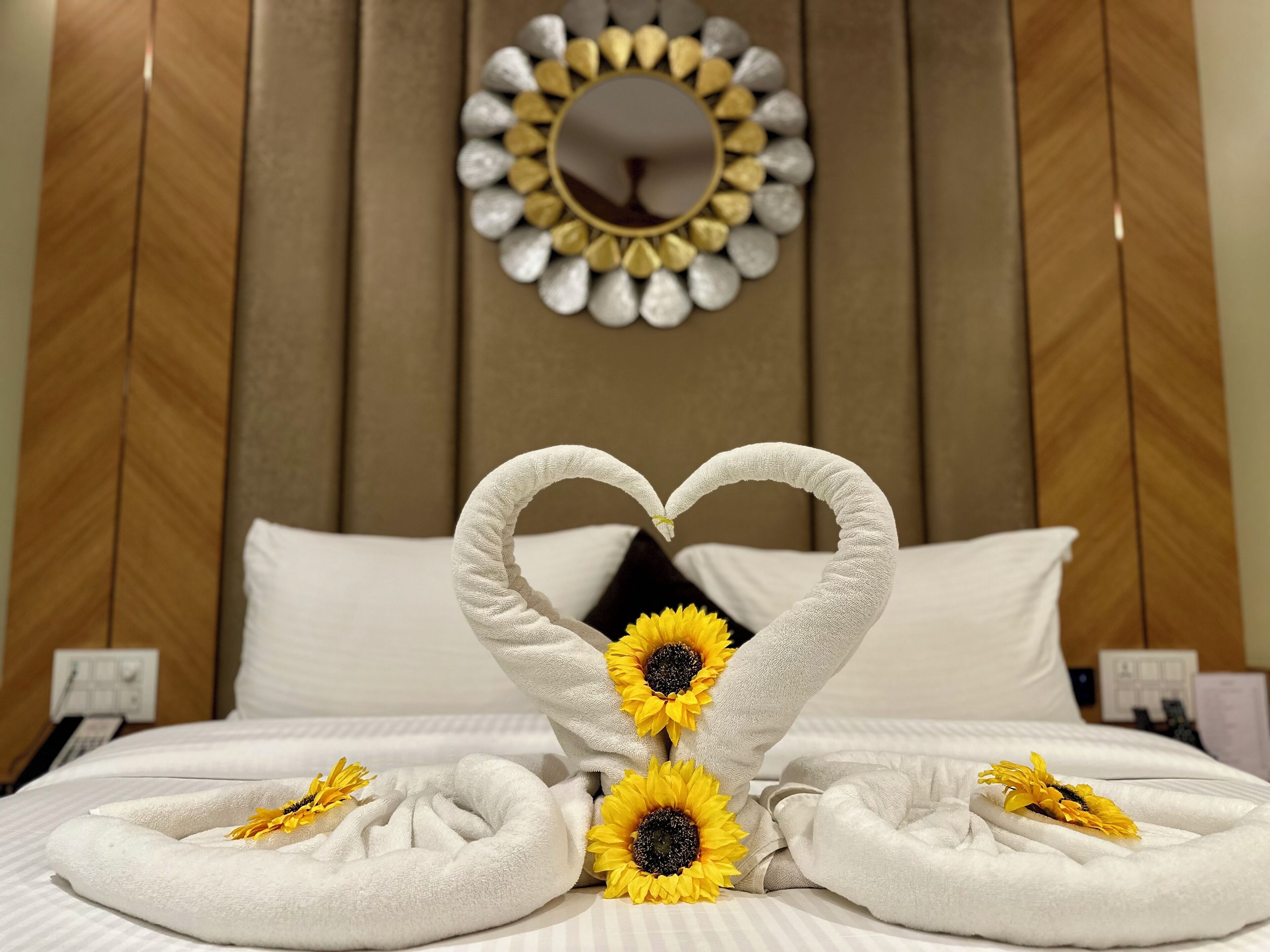 Una habitación de hotel con una cama, una toalla dispuesta en forma de corazón y girasoles.
