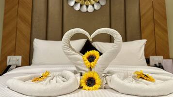 Una habitación de hotel con una cama, una toalla dispuesta en forma de corazón y girasoles.