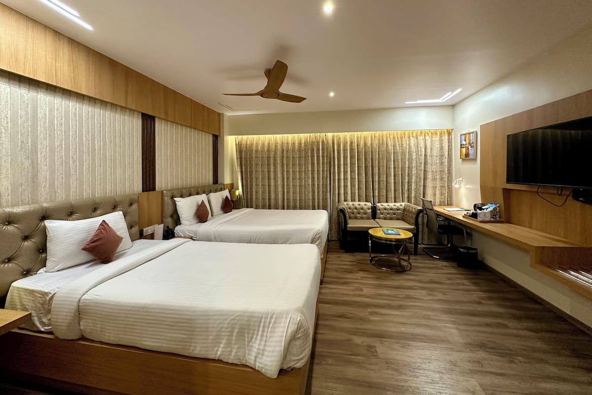 A hotel room with two beds, a sofa, a TV, and a ceiling fan.