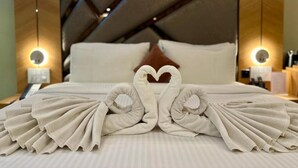 Habitación de hotel con una cama bien hecha, una toalla dispuesta en forma de corazón y un diseño moderno con detalles de madera e iluminación ambiental.