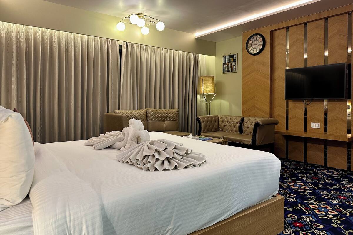 A hotel room with a large bed, a sofa, a television, and a clock on the wall.