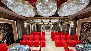 Un salón de banquetes con sillas y mesas rojas, grandes candelabros y paneles decorativos en las paredes.