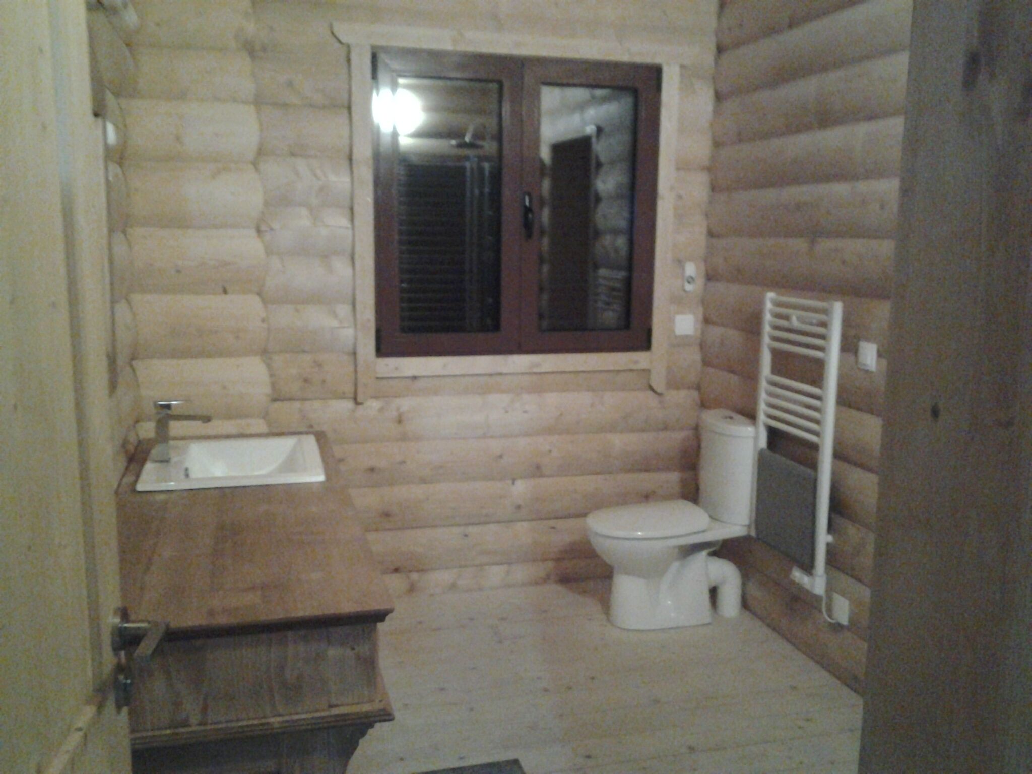 Un bagno piccolo e compatto con una parete in legno, un lavandino, un water e una finestra.
