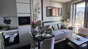 Een moderne keuken met een eethoek, een grijze bank en uitzicht op bergen door grote ramen.