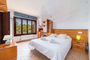 A hotel room with a large bed, a desk, a chair, a nightstand, a lamp, and a view of trees through the window. - Ca Na Xilla Alcanada 8 people pool (Alcúdia)