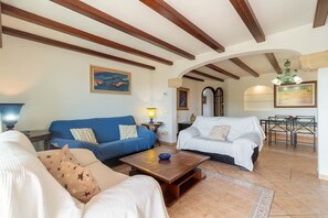 Ein Wohnzimmer mit blauem Sofa, weißem Sofa und Couchtisch aus Holz. An der Wand hängt ein Gemälde und auf einem Beistelltisch steht eine Lampe.