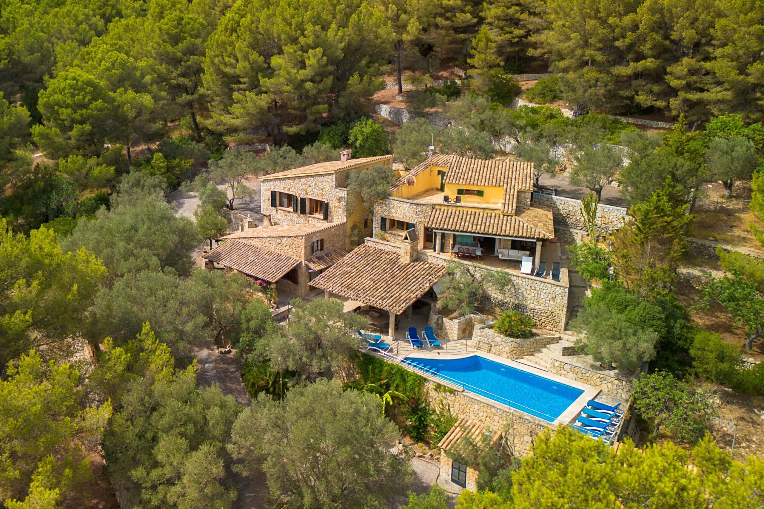 Una villa de estilo mediterráneo con piscina, rodeada de abundante vegetación.