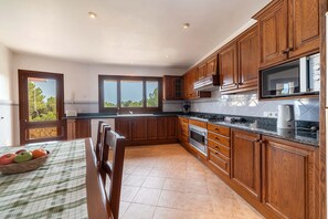 A kitchen with wooden cabinets, a stove, a microwave, and a dining table with a placemat. - Ca Na Xilla Alcanada 8 people pool (Alcúdia)