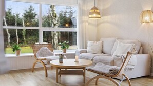 Una sala de estar moderna con un sofá, dos sillones, una mesa redonda y un ventanal con vistas a árboles.