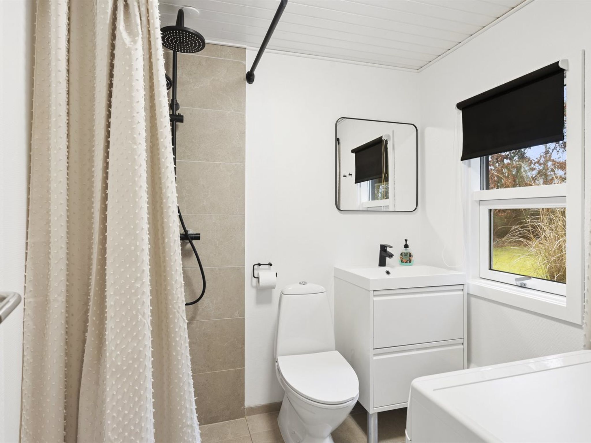 A bathroom with a shower, toilet, sink, and window.