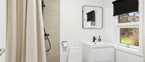 A bathroom with a shower, toilet, sink, and window.