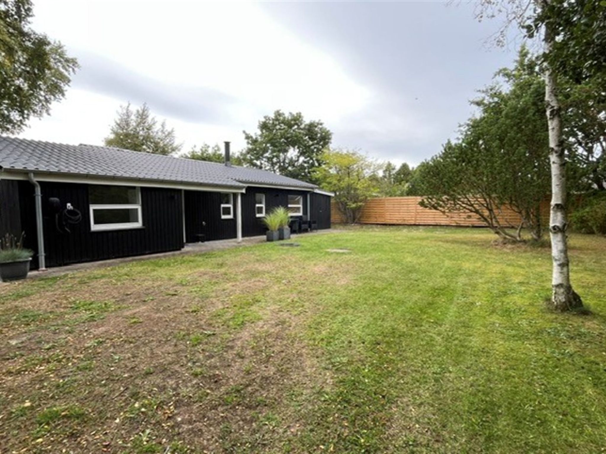 A black building with a sloped roof, a grassy yard, and a wooden fence.
