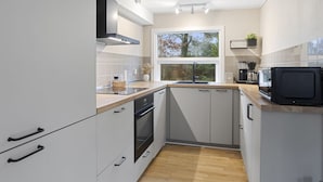 Una cocina moderna con muebles blancos, horno empotrado, microondas y ventana que proporciona luz natural.