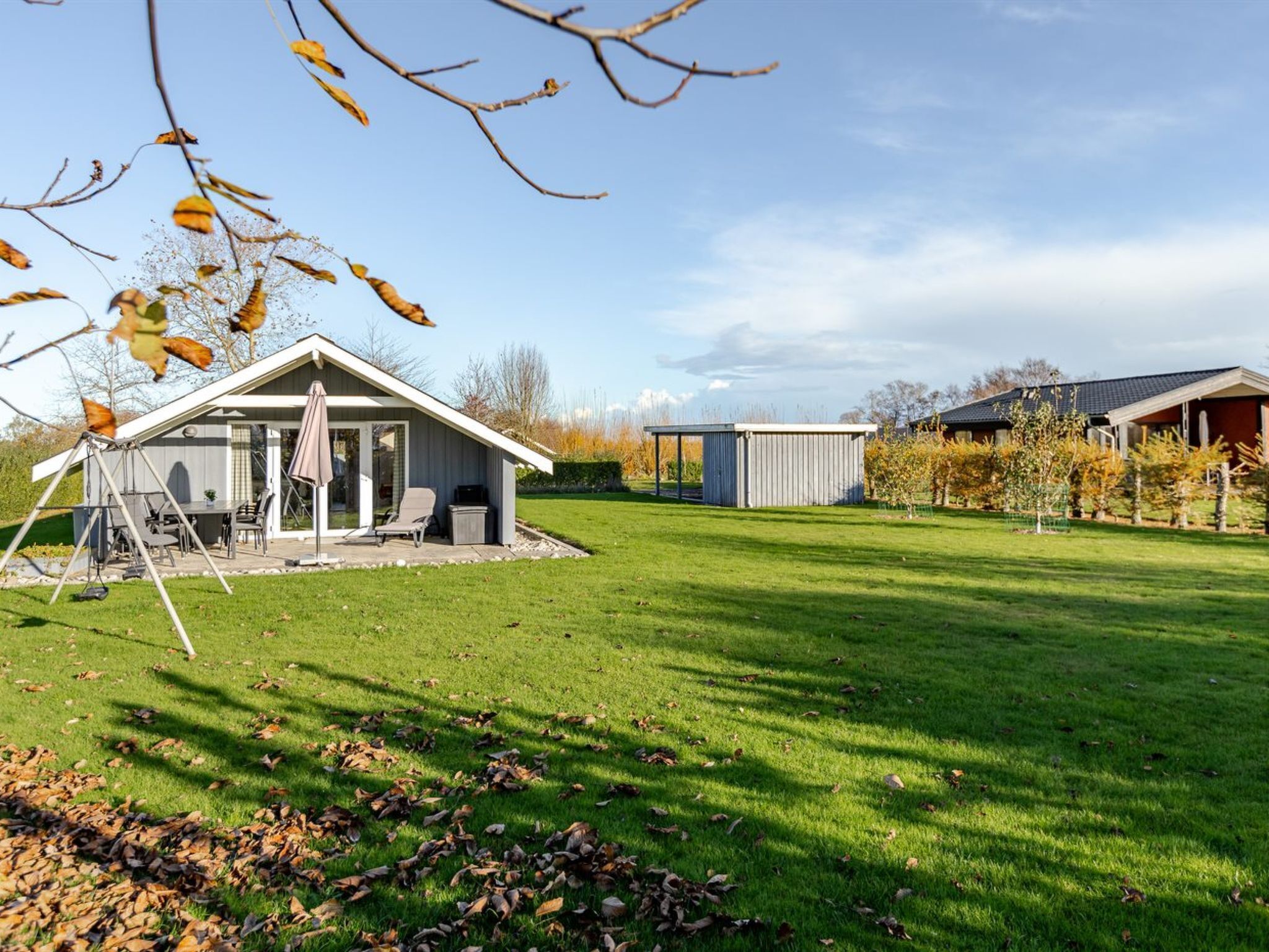 Een woonhuis met een overdekte patio, een schommel en een omheinde tuin.