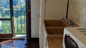 Una cocina equipada con lavadora, microondas y lavaplatos. Hay un balcón con vistas a las colinas.