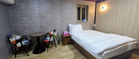 A hotel room with a bed, a small table, two chairs, a bedside table with a tissue box, and a wall-mounted light.