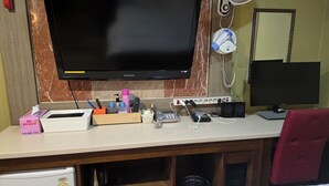 A hotel room with a flat-screen TV, a desk with various items including a phone, a speaker, and a keyboard. - Sky Motel (Gumi)