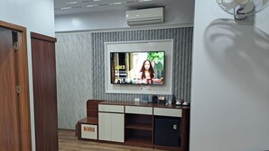 A modern living room with a flat-screen TV mounted on the wall, a wooden cabinet, a small fridge, and leather seating. - Hoang Gia Luxury (Hanoi)