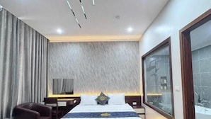 A modern bedroom with a large bed, a leather ottoman, a desk, and a large window. - Hoang Gia Luxury (Hanoi)