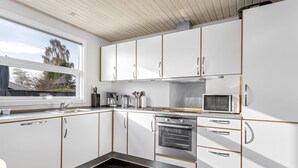 Ett modernt kök med vita skåp, en inbyggd ugn, en mikrovågsugn och en kaffebryggare.