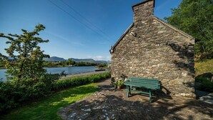 A stone building with a chimney, a bench, and a view of a lake and mountains. - Pier Cottage Sneem (Sneem)