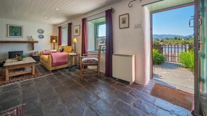 A cozy living room with a fireplace, a yellow sofa, a table, and a view of the outdoors. - Pier Cottage Sneem (Sneem)