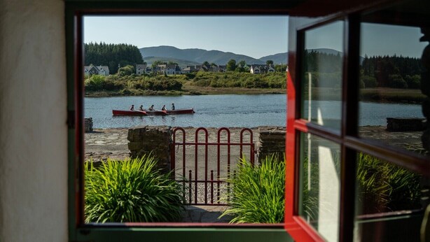 A view from inside a room looking out to a river with canoes, a stone wall, and greenery. - Pier Cottage Sneem (Sneem)