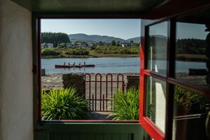 Uitzicht vanuit een kamer op een rivier met kano's, een stenen muur en begroeiing.